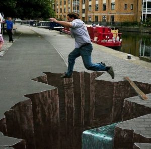A man jumping over what appears to be a giant hole in the sidewalk. In reality, it's sidewalk chalk art, and there is no hole.