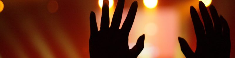 2 hands held up in worship against a red background